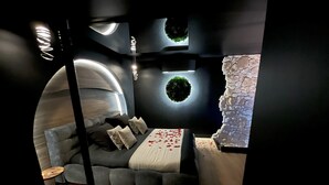 Une chambre moderne avec un plafond incurvé, un mur d’accent en pierre et un lit parsemé de pétales de rose.