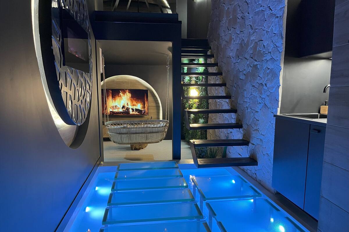 A modern interior with a glass floor leading to a lower level, a stone wall with greenery, and a fireplace.