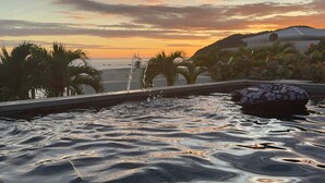 Une piscine avec des jets d’eau, des palmiers et une vue sur le coucher de soleil.