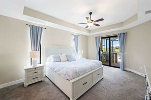 A bedroom with a bed, nightstands, a ceiling fan, and a view of the outdoors.