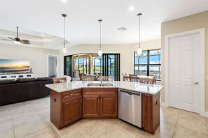 A modern kitchen with a central island, built-in appliances, and a dining area with a view. - Peaceful Breeze (Cape Coral)