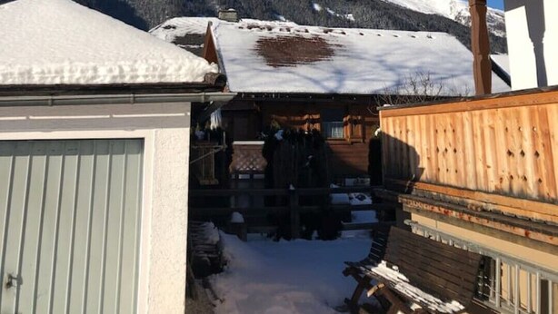 Un edificio de madera con balcón, techo cubierto de nieve y montañas al fondo.