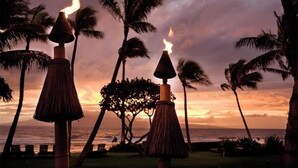 Une vue au coucher du soleil, avec des parasols en chaume et des palmiers.