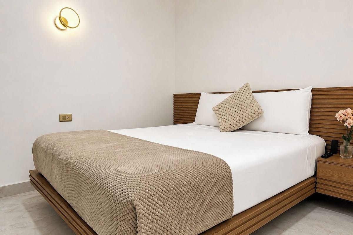 A neatly made bed with a textured blanket, a wooden headboard, and a bedside table with a vase of flowers.