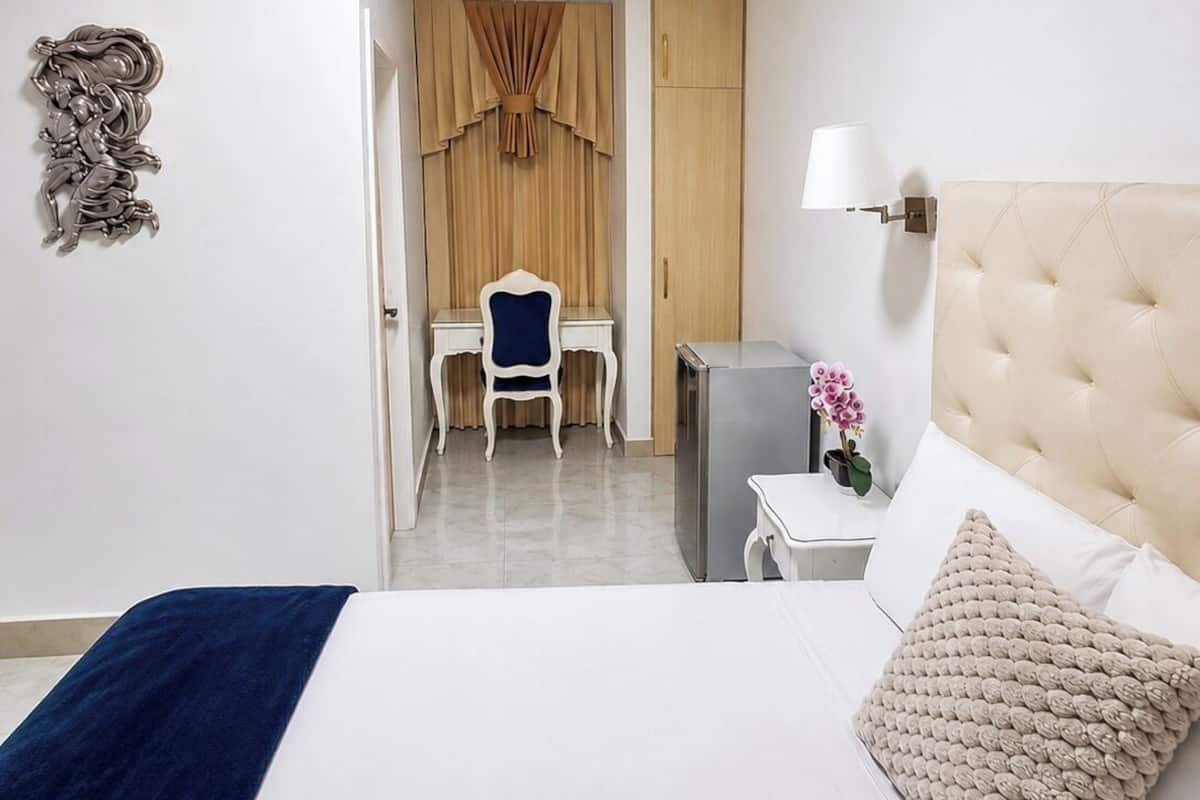 A hotel room with a bed, a desk, a chair, a lamp, and a wardrobe.