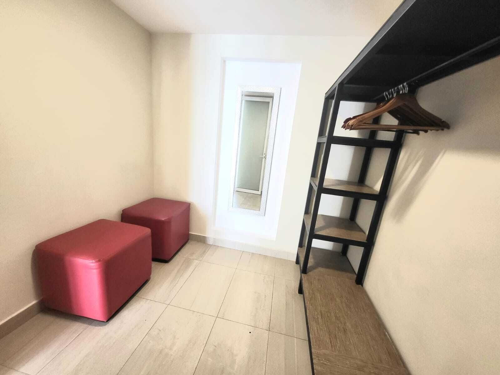 Een kleine, lichte kamer met een betegelde vloer, een witte deur en een zwart metalen rek met een kleerhanger.