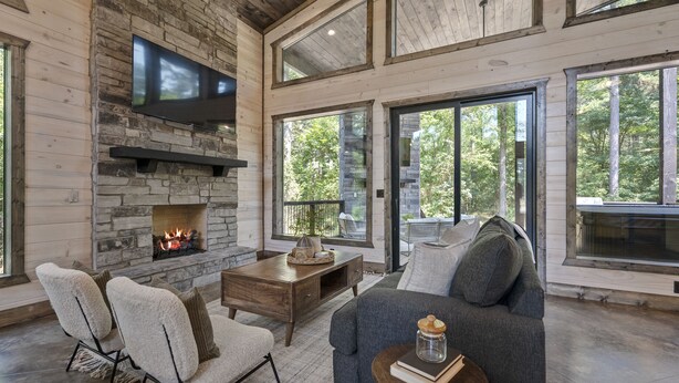 A cozy living room with a stone fireplace, comfortable seating, and large windows offering a view of the outdoors.