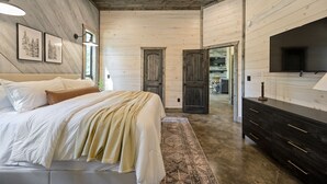 A bedroom with a bed, bedside tables, a dresser, a TV, and a door leading to another room.