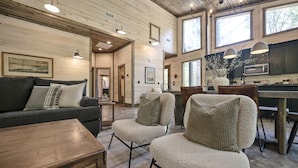 A cozy living room with a sofa, chairs, a wooden coffee table, and a kitchen area with cabinets and a dining table.