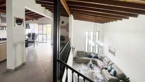A spacious living area with a high ceiling and exposed wooden beams, a comfortable sofa set, and a dining area with chairs and a table.