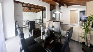 A modern dining area with a glass table, black chairs, and a wooden ceiling.