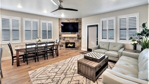 A spacious living room with a fireplace, a television mounted on a stone wall, and a ceiling fan.
