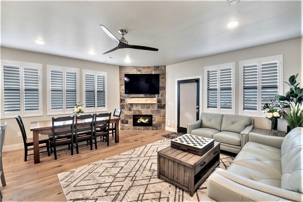 A spacious living room with a fireplace, a television mounted on a stone wall, and a ceiling fan.