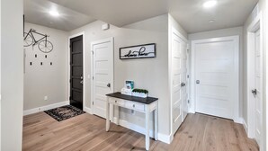 A hallway with a white door, a welcome home sign, a small table with a plant, and a bicycle mounted on the wall.