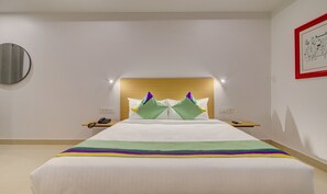 Een hotelkamer met een groot bed, een houten hoofdbord, nachtkastjes met lampen, een telefoon en een ingelijst schilderij aan de muur.