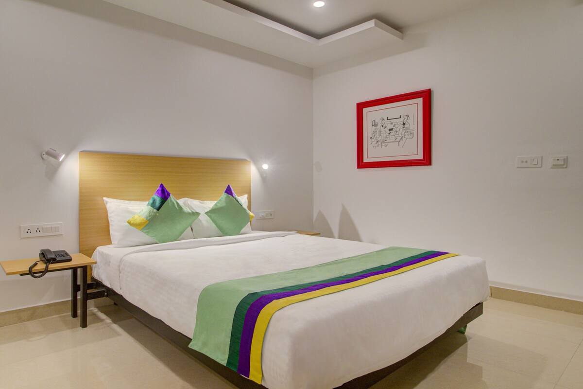A neatly made bed with a wooden headboard, a bedside table with a telephone, and a framed picture on the wall.