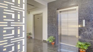 A modern elevator with a metallic finish, a marble wall, and a geometric decorative panel. - Treebo De Alphabet Kondapur (Hyderabad)