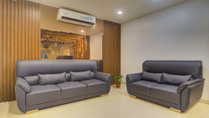 A modern living room with two grey sofas, a wooden accent wall, and an air conditioning unit. - Treebo De Alphabet Kondapur (Hyderabad)