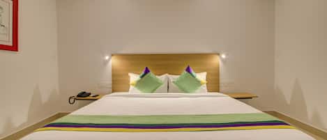Un cuarto de hotel con una cama grande, un cabecero de madera, una mesita de noche con un teléfono y un cuadro enmarcado en la pared.
