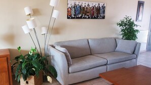 Una sala de estar con un sofá gris, una mesita de madera, una planta y un cuadro en la pared.