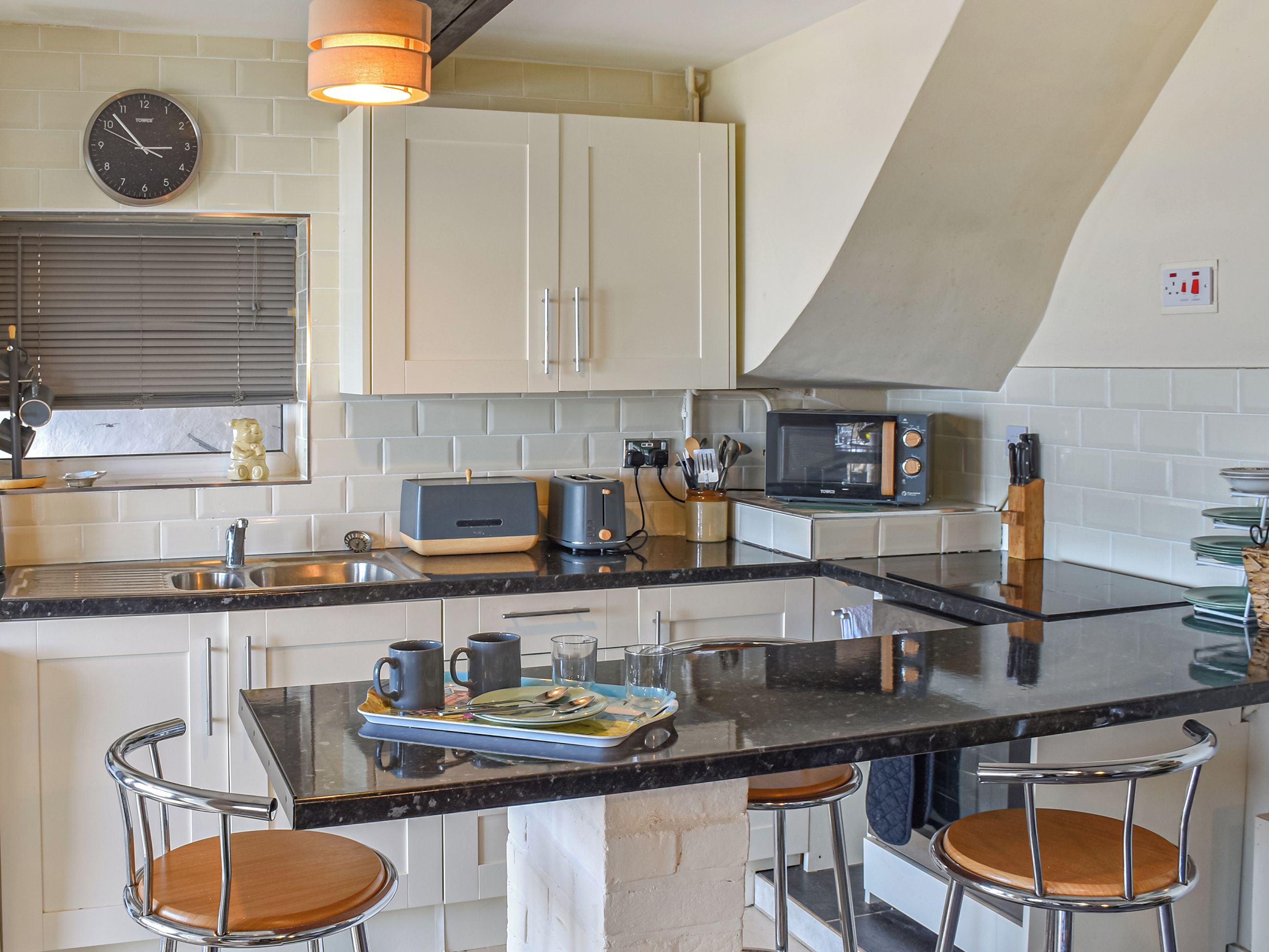 Une cuisine avec un îlot central, des tabourets de bar, un four à micro-ondes, un grille-pain et une horloge murale.