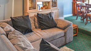 A cozy living room with a sofa, a cabinet with glass doors, and a dining area with chairs. - 1 bedroom accommodation in Sheringham (Sheringham)