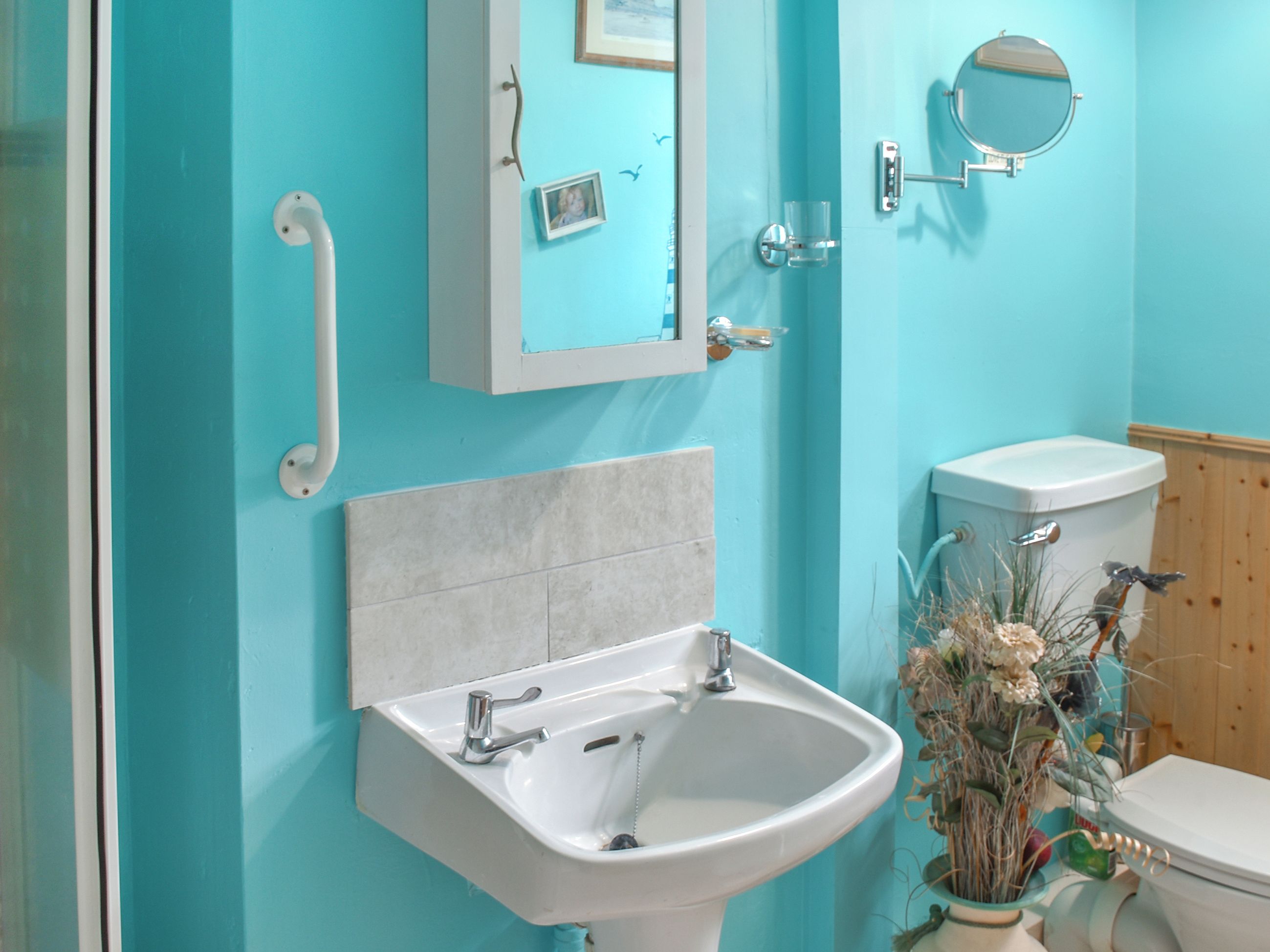 A bathroom with a white sink, a mirror, a toilet, and a handrail.