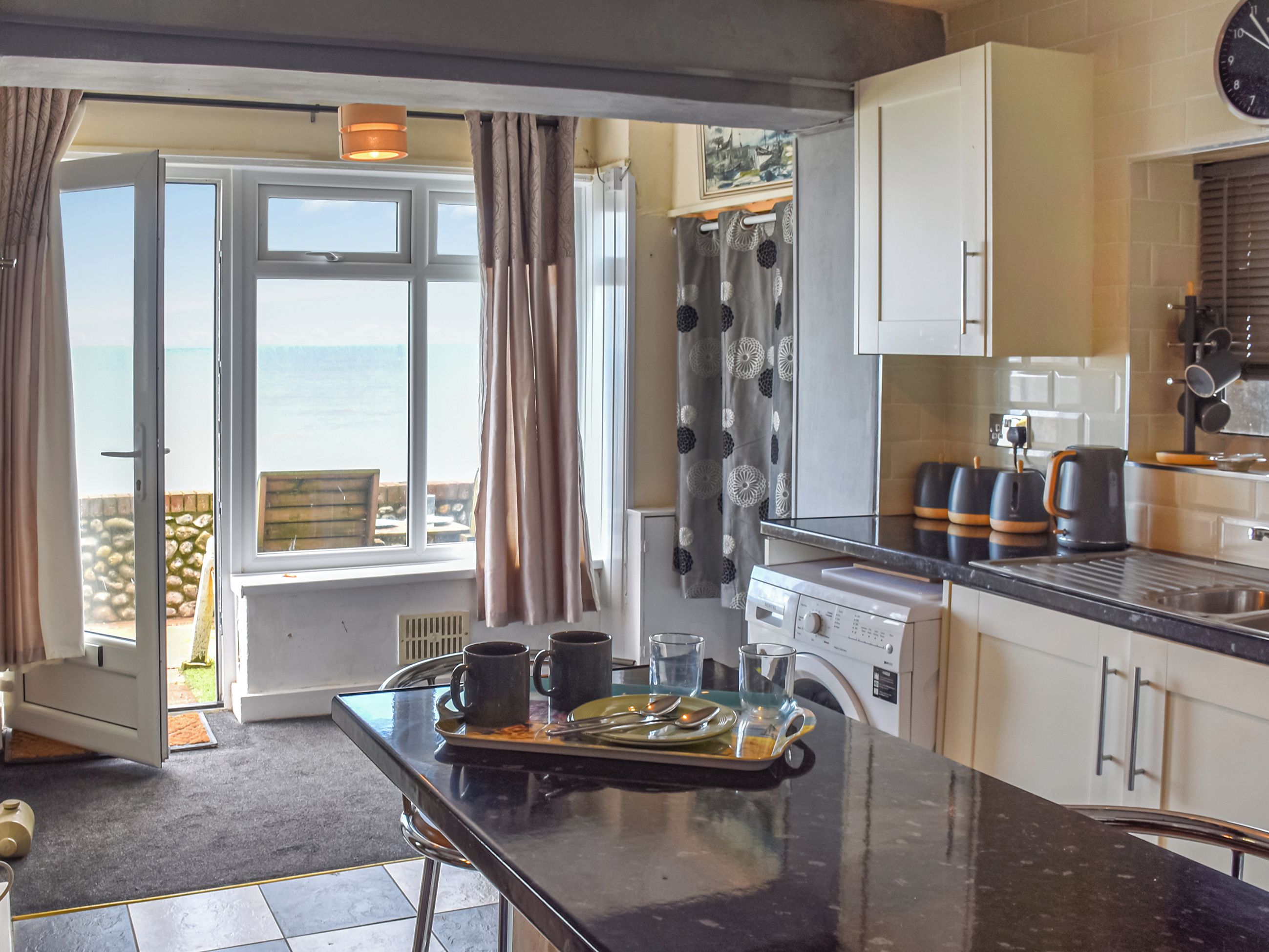 A kitchen with a view of the sea, a dining area with a table set for two, and a washing machine.