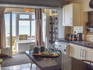 A kitchen with a view of the sea, a dining area with a table set for two, and a washing machine.