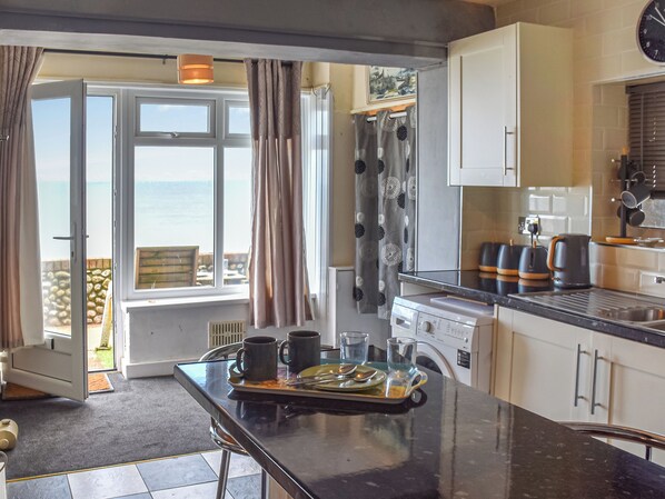 A kitchen with a view of the sea, a dining area with a table set for two, and a washing machine.