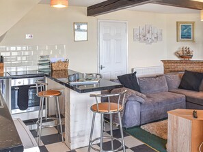 A kitchen with a central island, bar stools, a built-in oven, and a dining area with a sofa and a fireplace. - 1 bedroom accommodation in Sheringham (Sheringham)