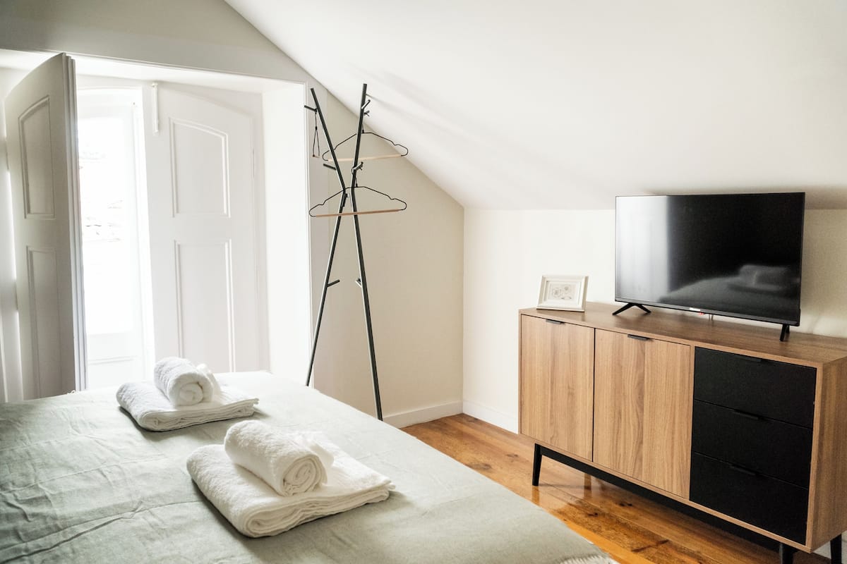 Ein Schlafzimmer mit einem Bett, einem Fernseher auf einem Holzschrank, einem Kleiderständer und einer Tür zu einem anderen Raum.