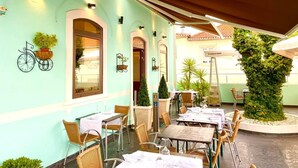 Un café en plein air avec des tables et des chaises, des plantes en pot et une décoration représentant un vélo sur le mur.