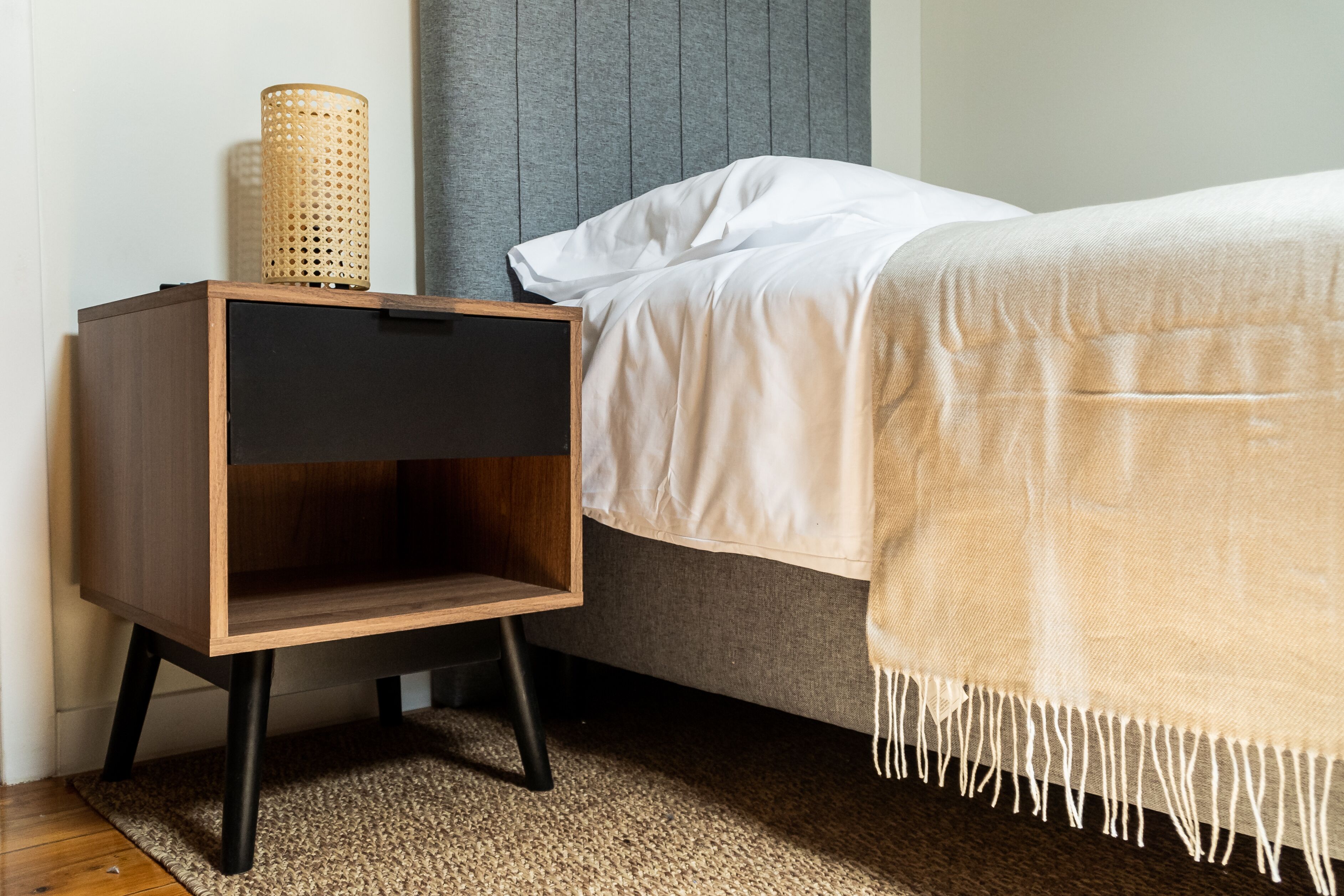 A neatly made bed with a white comforter and a beige throw blanket.