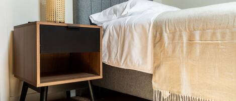 A neatly made bed with a white comforter and a beige throw blanket.