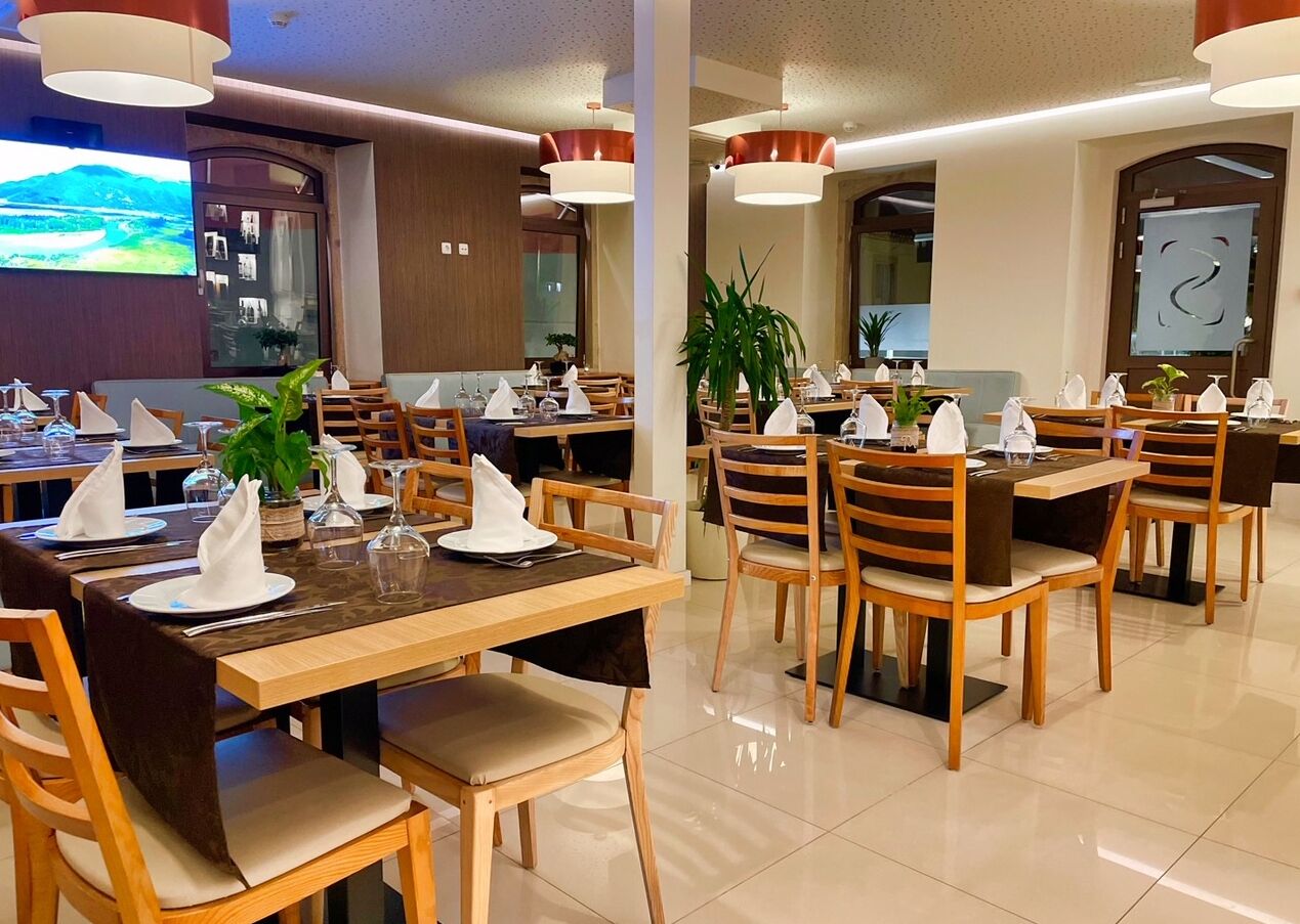 A hotel dining area with multiple tables, chairs, and a television screen in the background.