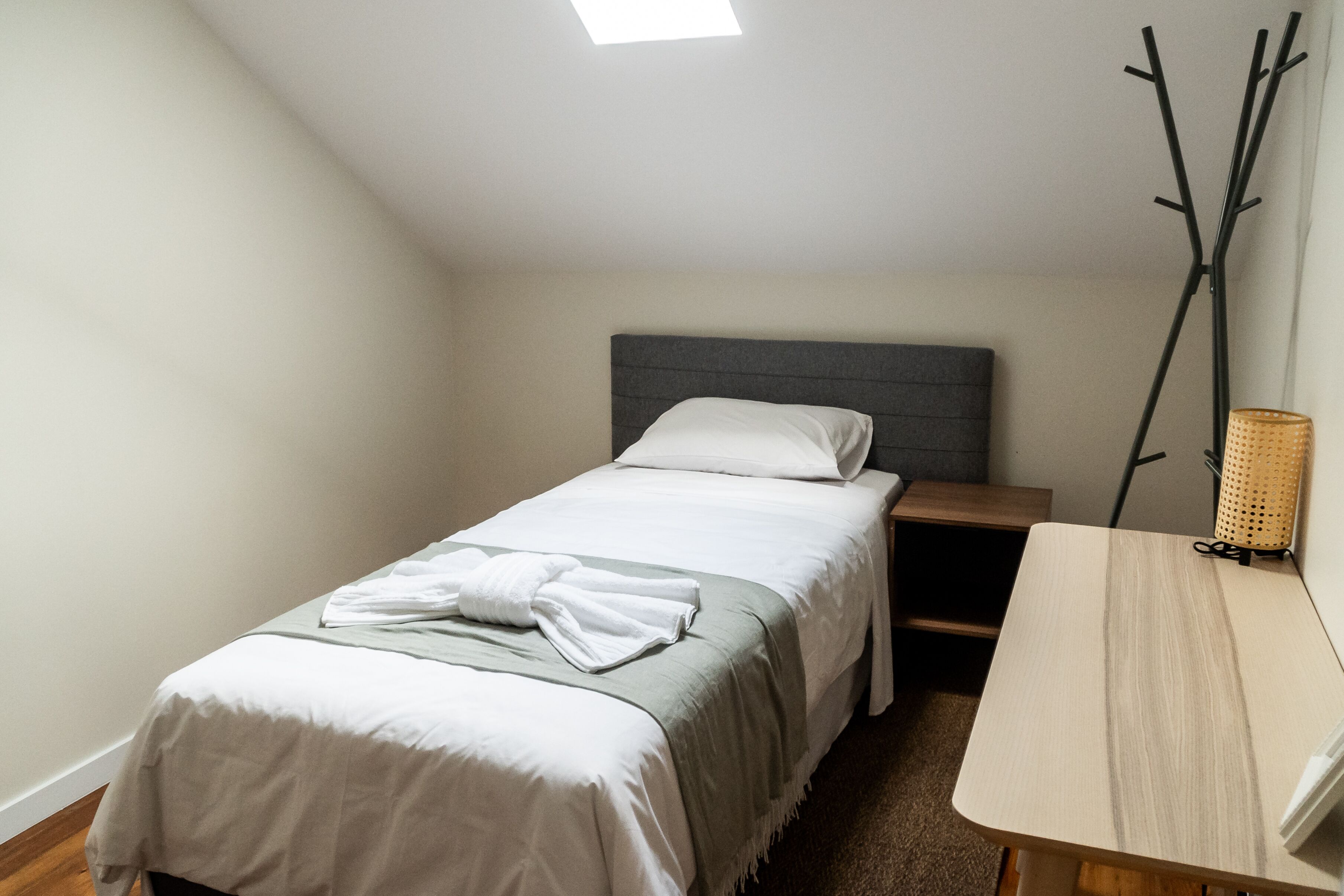 A small, neatly arranged bedroom with a single bed, a bedside table, and a lamp.