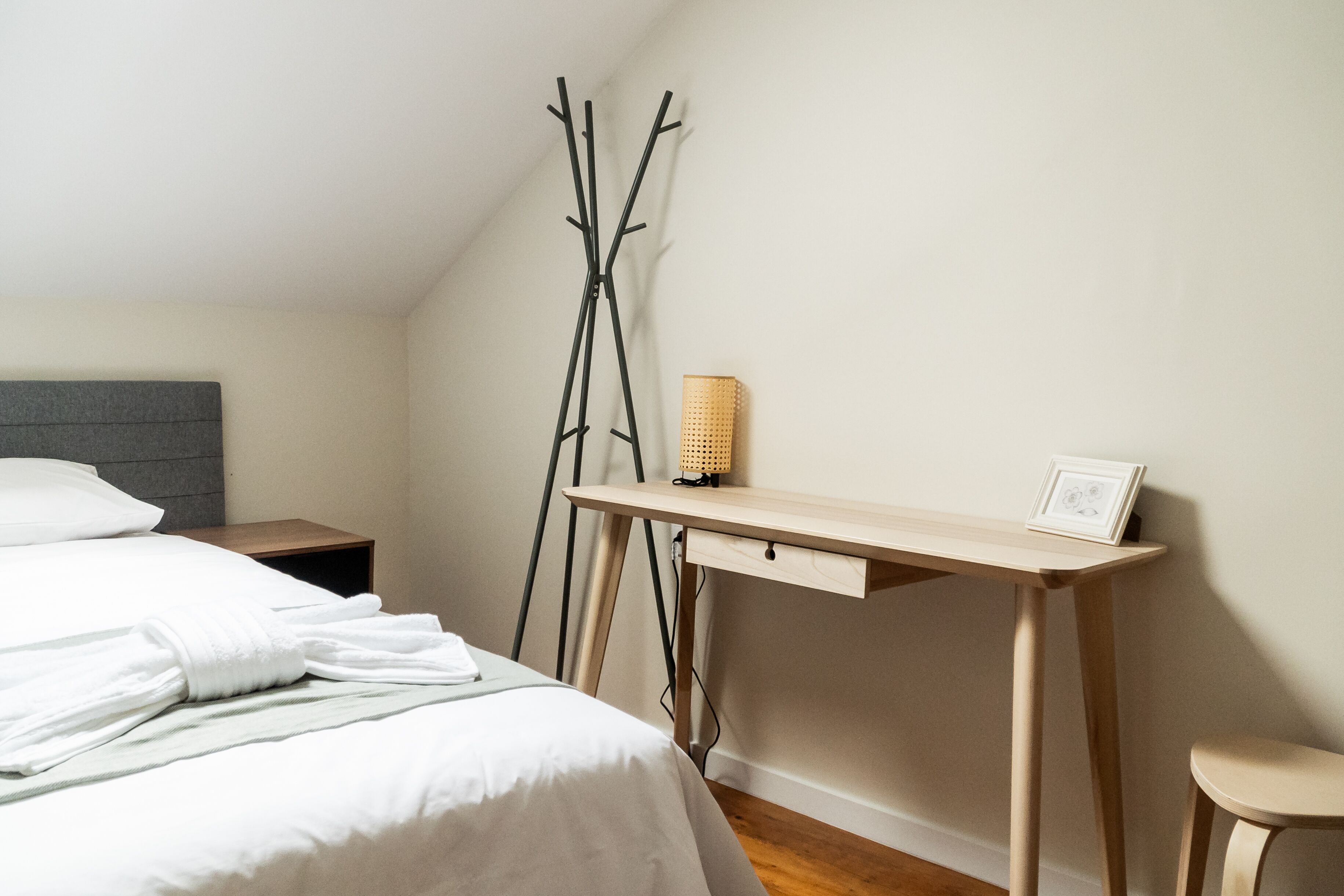 A bedroom with a bed, a desk, a chair, and a bedside table.