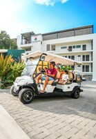 Un carrito de golf con pasajeros, estacionado frente a un hotel con un letrero que dice 'La Puesta Sayulita'.
