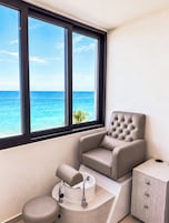 Habitación con vista al océano, un sillón con textura, un lavamanos pequeño y un armario de madera.