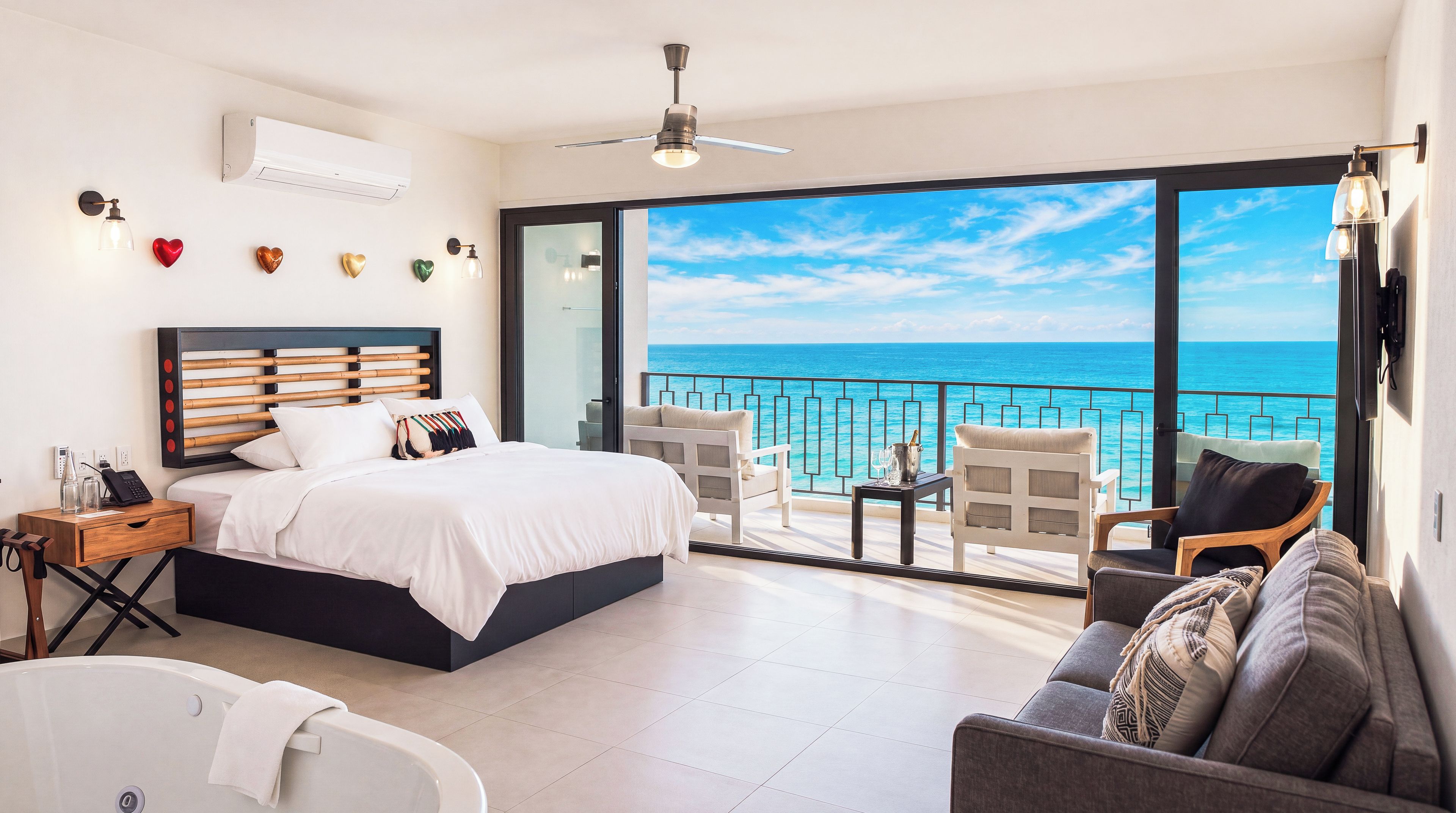 A modern bedroom with a large bed, a balcony with a view of the sea, and a seating area with a view.