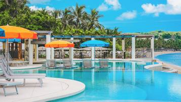 A pool area with lounge chairs and umbrellas, surrounded by palm trees and a view of the beach.