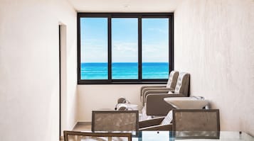 Una habitación con un amplio ventanal con vistas al océano, una mesa de vidrio y dos sillones acolchados.