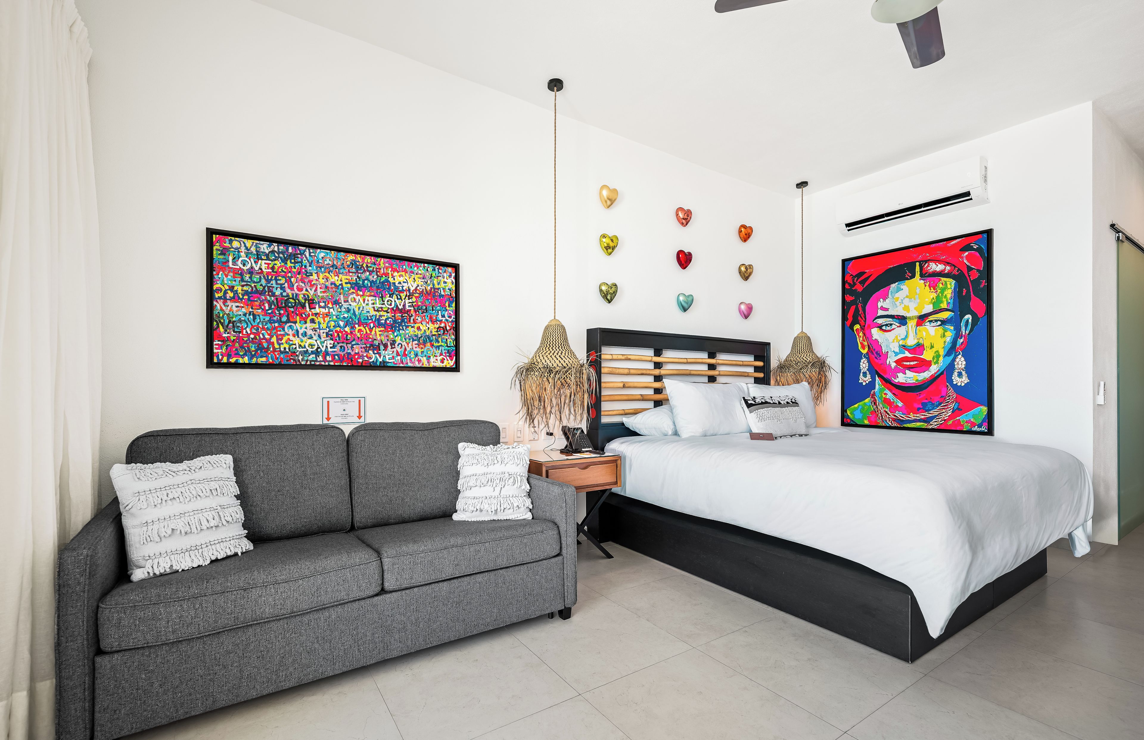 Un dormitorio moderno con un sofá gris, una cama con ropa de cama blanca y dos obras de arte colgadas en la pared.