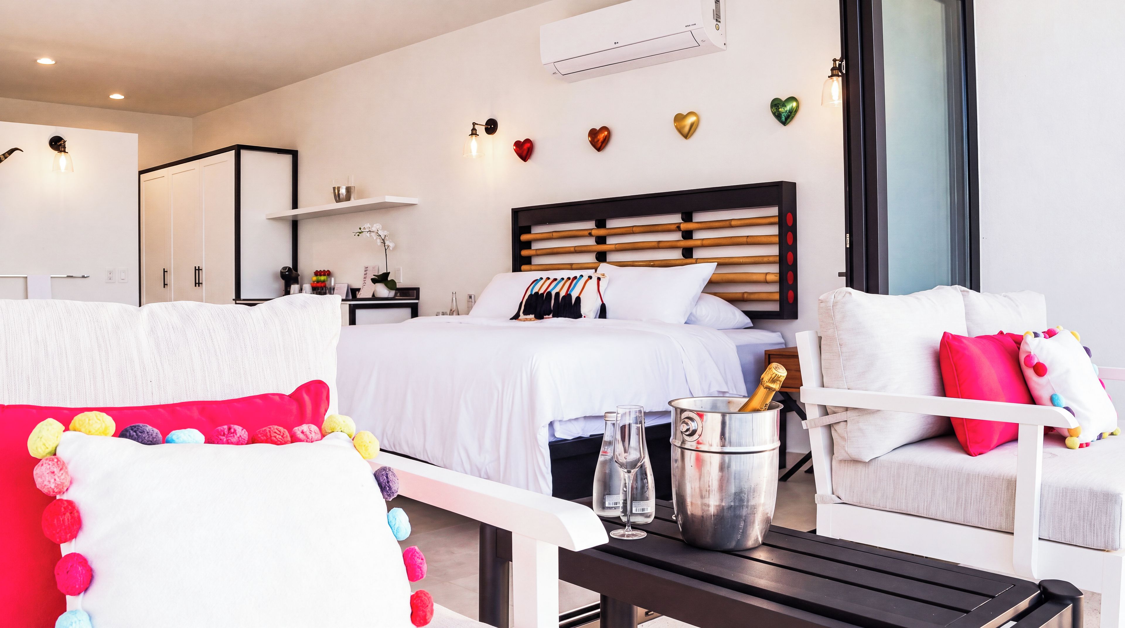 A modern hotel room with a bed, a seating area, a minibar, and decorative heart-shaped wall art.