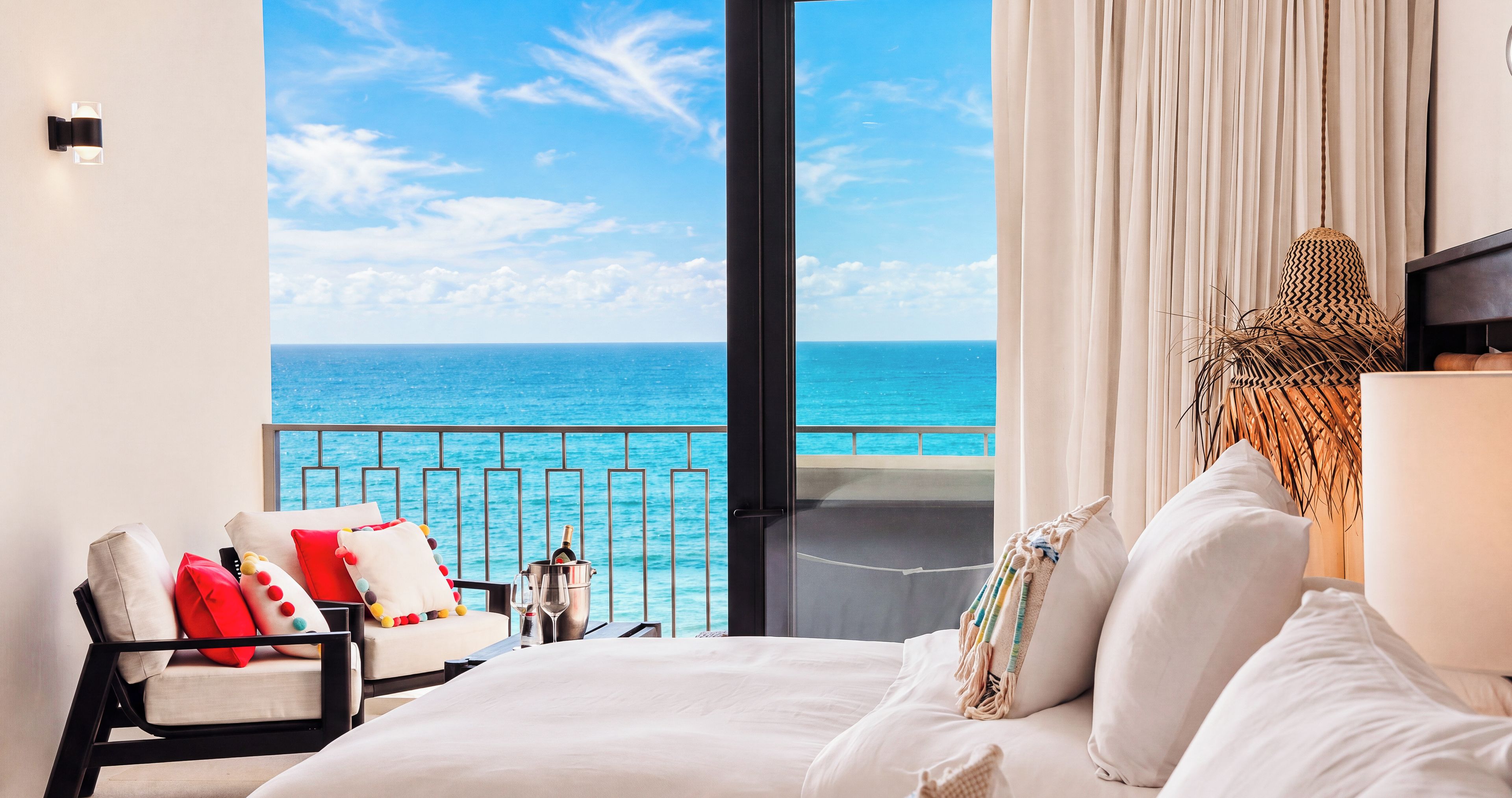 Habitación de hotel con balcón, cama, silla y vista al océano.