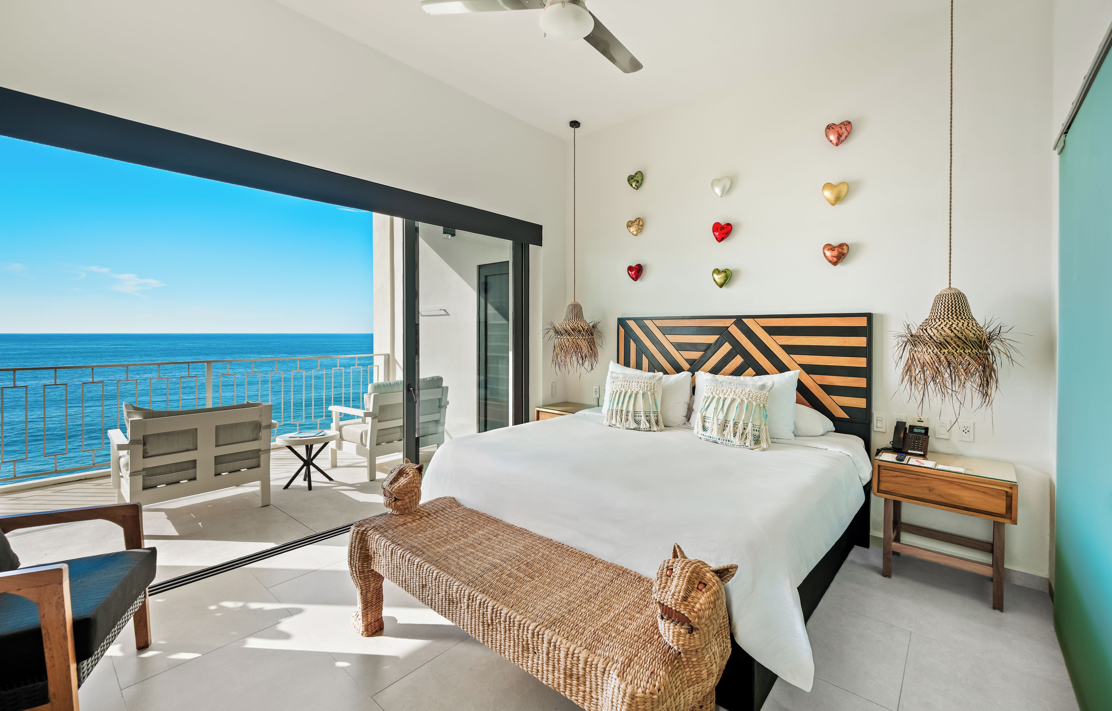 Un dormitorio moderno con una cama grande, vista al mar y decoración de corazones en la pared.