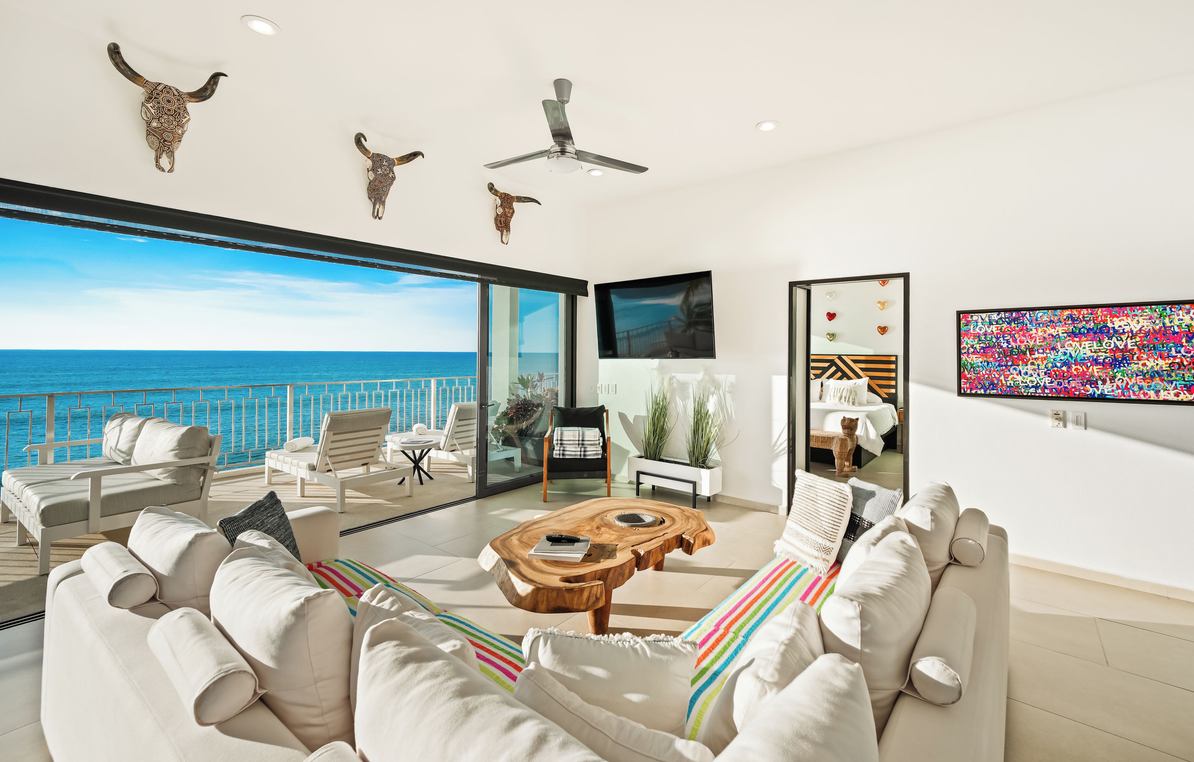 A modern living room with a view of the sea, a ceiling fan, and a flat-screen TV.