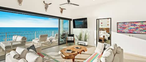 Un salon moderne avec vue sur la mer, doté d’un ventilateur de plafond et d’un téléviseur à écran plat.