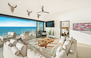 Una sala moderna con vista al mar, un ventilador de techo y un televisor de pantalla plana.